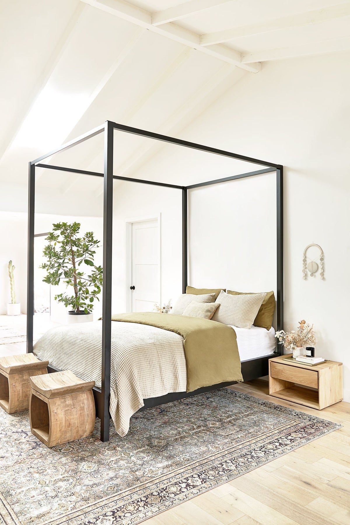 | Two devlin stools sit atop a traditional rug in a bedroom at the edge of a black-framed canopy bed