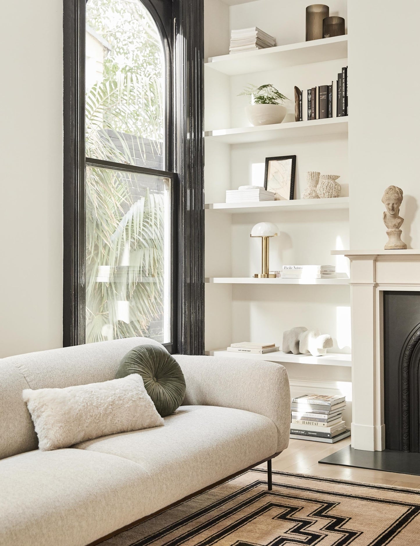 | The Lelani table lamp with half-moon shade on a gold base sits in a living room on a shelf with various sculptural objects